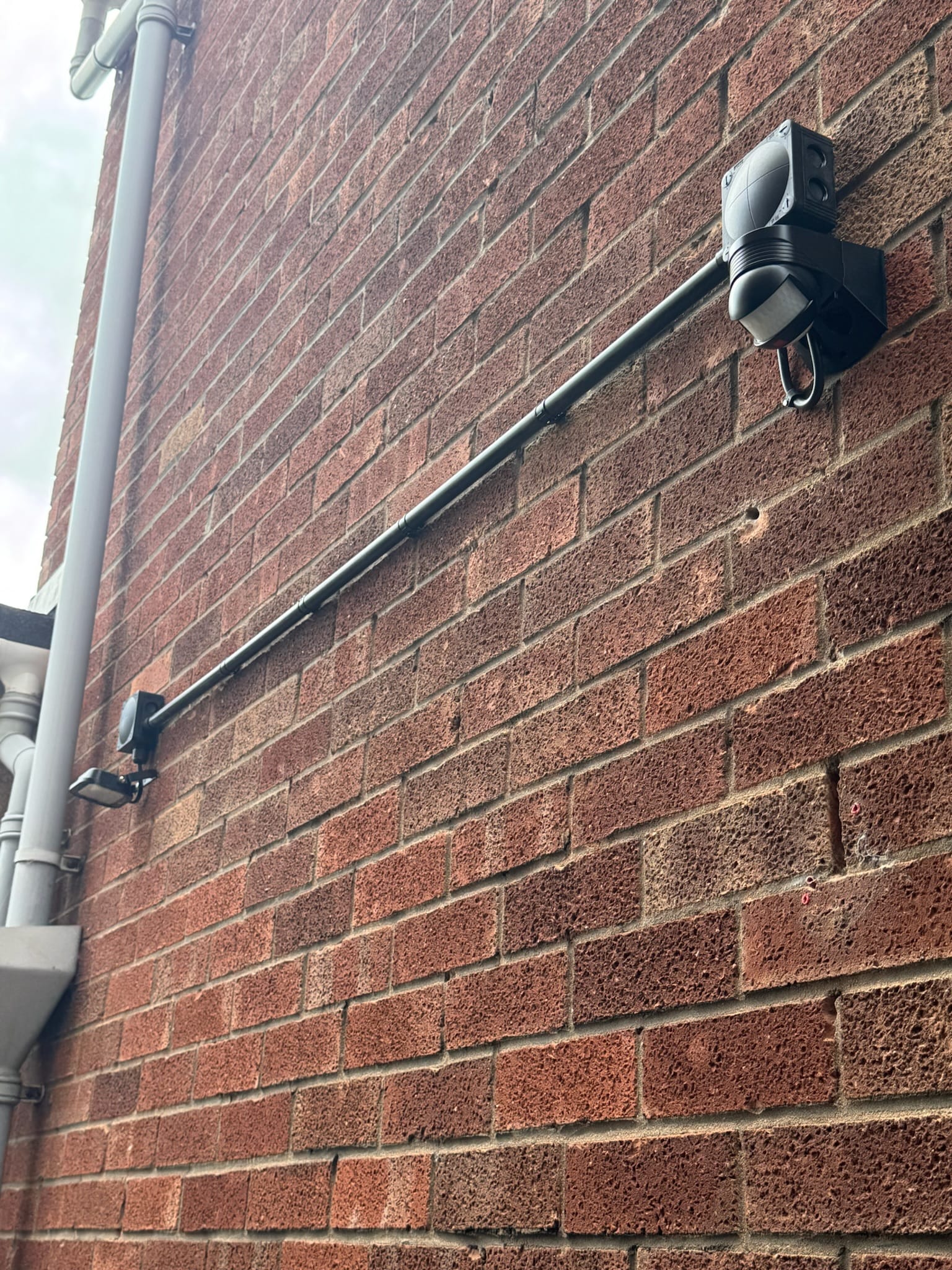 Completed security light installation in Bristol showing outdoor LED lighting, black conduit and a separate PIR motion sensor on a brick wall.